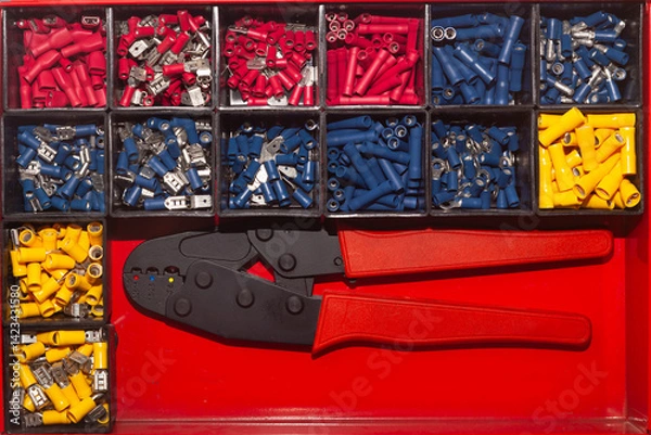 Obraz A box of new terminals for electrical wires of different colors and a special terminal clamp.