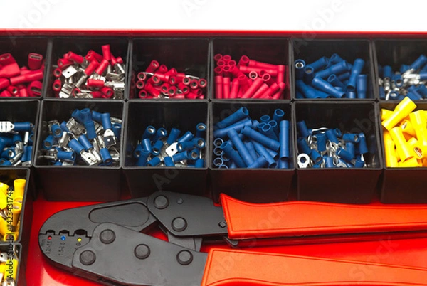 Obraz A box of new terminals for electrical wires of different colors and a special terminal clamp.