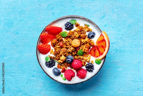 Fototapeta Granola with yogurt and fresh fruit. Organic gourmet muesli with ingredients, overhead flat lay shot on a blue background