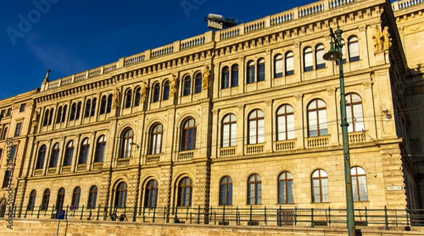 Fototapeta Facade of historic neoclassical building with arched windows and sculptures in Budapest, Hungary, illuminated by warm sunlight under clear blue sky