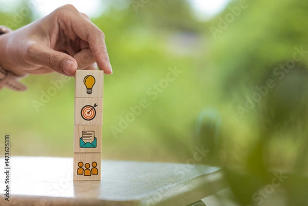 Obraz Another hand places a light bulb block on top of a pyramid of blocks, symbolizing building ideas and structured thinking.