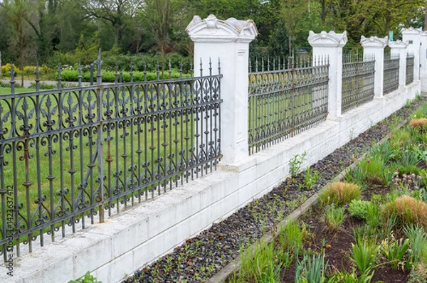 Fototapeta Wrought iron fence protecting lush green garden in spring