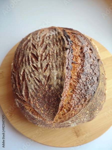 Fototapeta freshly baked artisanal sourdough bread with rustic crust cooling on a wooden surface side view