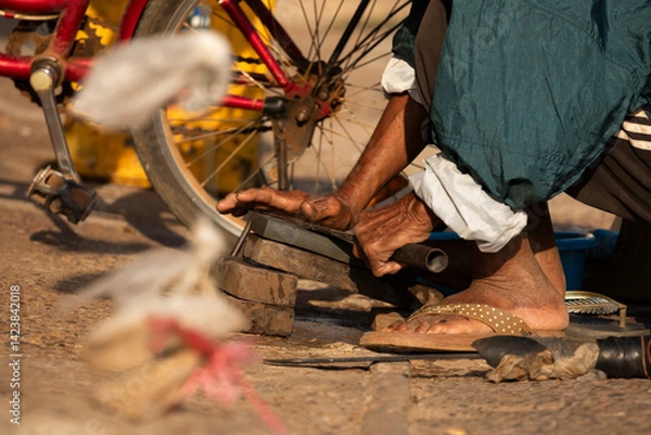 Obraz An elderly man works sharpening knives and machetes by hand, with a whetstone, at the Bai Don market in Pakse