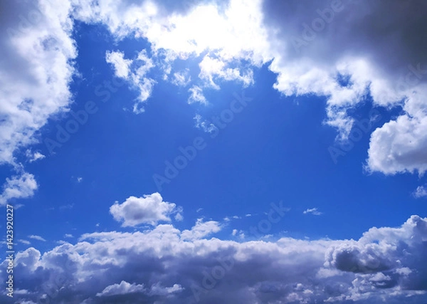 Obraz Bright blue sky framed by fluffy white and dark clouds. Inspiring, peaceful, and perfect for adding depth to design projects, websites, or marketing campaigns.
