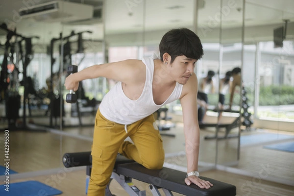 Obraz young handsome asian man works out exercise weights lifting in modern gym