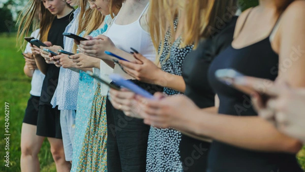 Fototapeta High school students bonding outdoors during summer, using smartphones to connect with friends and share experiences