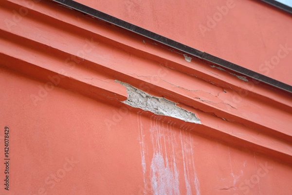 Fototapeta Detailed view of red building with damaged facade, importance of preservation. Damaged facade, weathering and paint peeling. Decaying red wall of building with broken surface, visible cracks