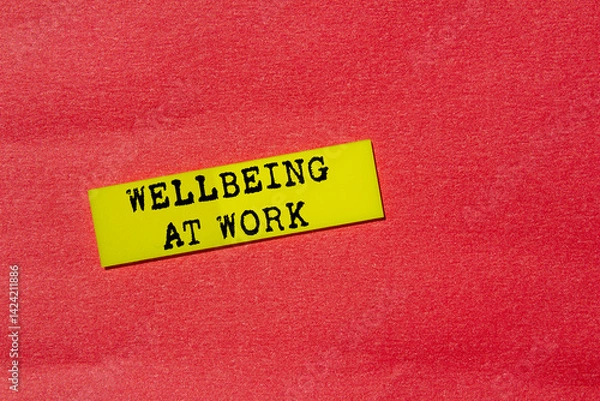 Fototapeta Wellbeing at work message written on yellow paper label on red background. Conceptual wellbeing at work symbol. Copy space.