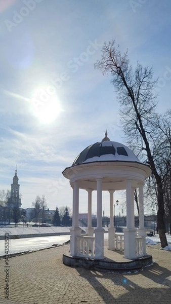 Fototapeta Rotunda on left bank of Orlik River with beautiful view of Cathedral of Archangel Michael in Orel city. Old white gazebo on background of river and Orthodox church on sunny winter day