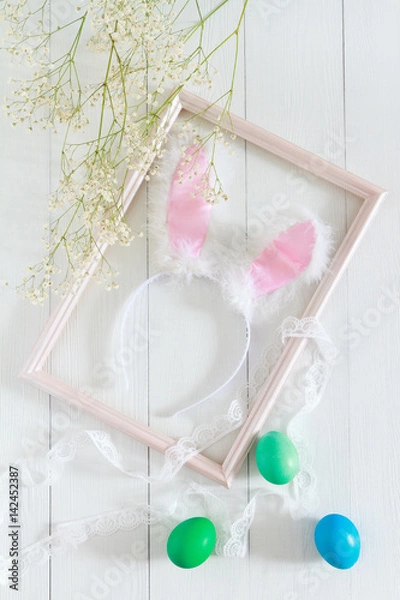 Obraz Easter bunny ears in a frame for pictures and colorful eggs on a white background. Top view and space for text