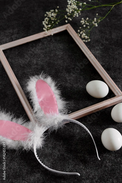 Obraz Easter bunny ears in a frame for pictures and eggs on a black background. Side view and space for text