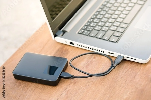 Obraz Technology concept : External hard disk and laptop computer with warm light effect. External hard drive connected to laptop on wooden table with copy space.
