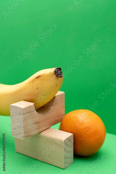 Obraz Still life with wooden blocks, tangerine and banana on a green background	