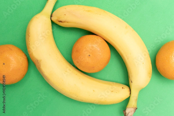 Obraz Bananas and tangerine on a green background