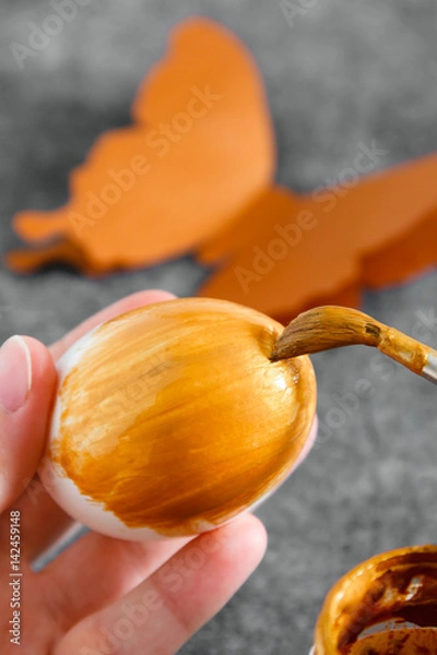 Fototapeta Workspace with easter decoration. Woman paints Easter eggs, slide view. Selective focus
