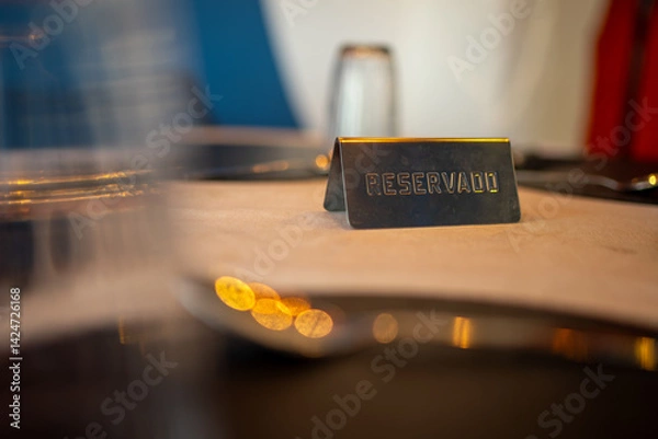 Fototapeta Metal reserved sign standing on an elegant restaurant table, creating an inviting atmosphere with soft, warm lighting and blurred tableware in the foreground and background