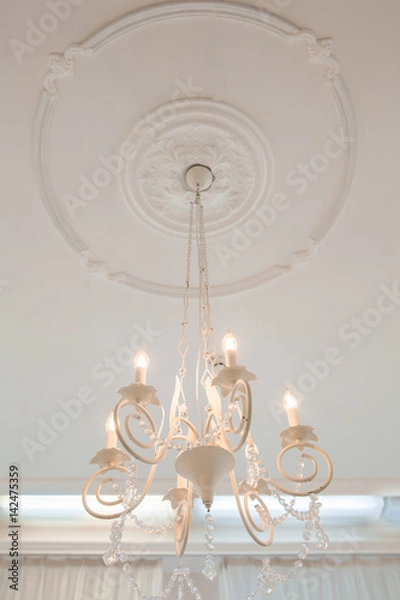 Fototapeta A view from below on a white chandelier hanging from a ceiling rose molding