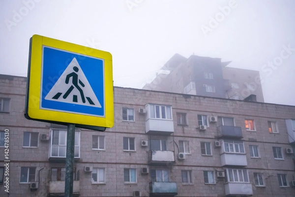 Fototapeta Pedestrian crossing sign on the background of an old multi-storey building with windows and balconies on a foggy rainy gray morning