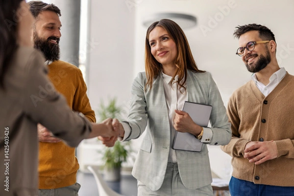 Fototapeta Female chief shaking hands with business partner while standing with her team of experts at office.