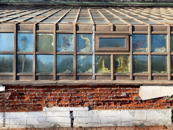 Fototapeta Fragment of abandoned greenhouse or orangery. Strong humidity and high heating temperatures led to rapid dilapidation of building. Construction design errors. Dilapidated building for demolished