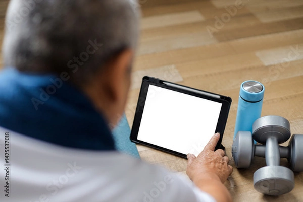 Obraz Senior sporty man in sportswear sitting on the floor and using laptop with blank screen after exercise