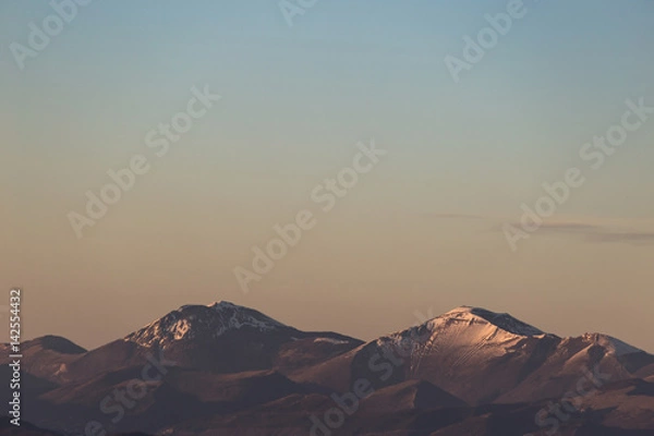 Fototapeta A minimalist view of some mountains top with snow, under a big, almost empty sky, with golden hour warm colors
