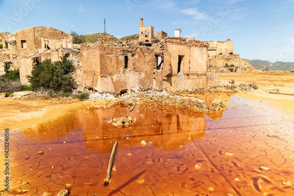 Obraz Abandoned mining ruins and cracked orange toxic pond in Mazarrón, Murcia, Spain, reflecting industrial decay, environmental contamination, and surreal desert transformation under harsh sunlight