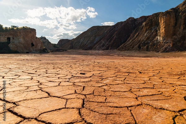 Obraz Cracked parched earth with oxidized mineral cliffs under blue sky at Mazarrón mines in Murcia, Spain, illustrating drought, environmental decay, and geological transformation