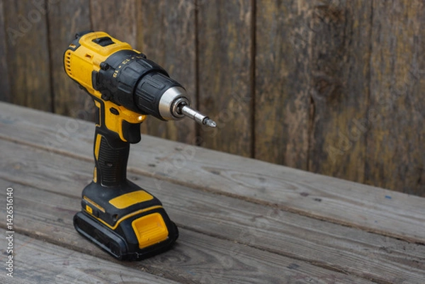 Fototapeta Yellow Cordless power drill on wooden surface for construction, DIY, and home repair projects.