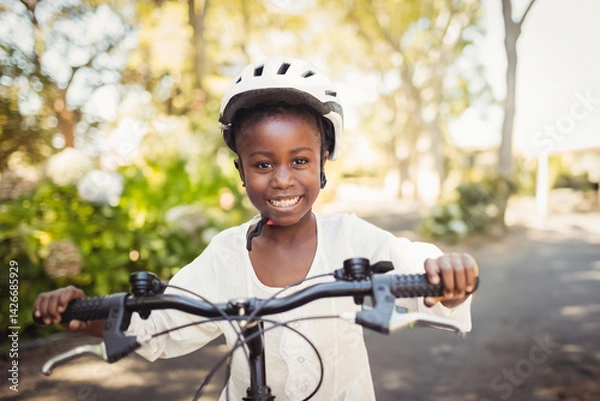 Obraz African American child gripping bicycle handlebars while wearing protective helmet on suburban road