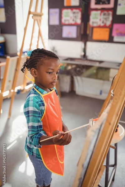 Obraz African American child painting on easel in art classroom, with paintbrush and canvas, copy space