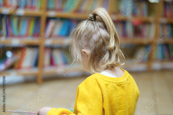Fototapeta Child reading in a colorful library surrounded by shelves filled with books during daytime