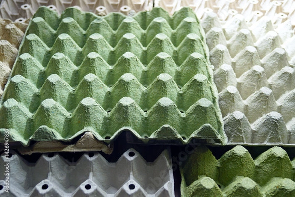 Fototapeta Sustainable development principles: using recycled packaging in the food industry. Gray and green egg cartons made from waste paper laid out on a surface. Large pulp trays for eggs illuminated by sun
