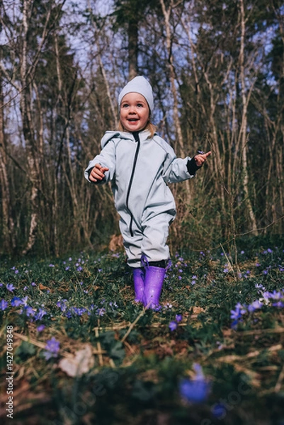 Obraz Little girl in violet boots and blue overall walking in spring blooming forest