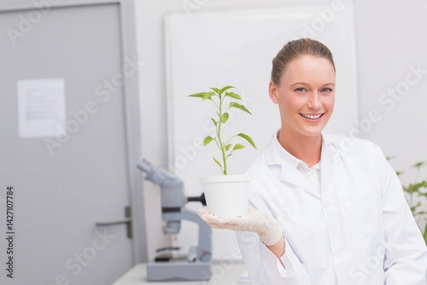 Fototapeta female scientist wearing lab coat, gloves, holding white pot with seedling in lab with microscope