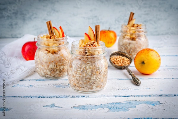 Fototapeta Overnight no-cooked oatmeal breakfast - Oats soaked in almond milk with cinnamon, crushed almond nuts and apple topping served as close-up in a jar