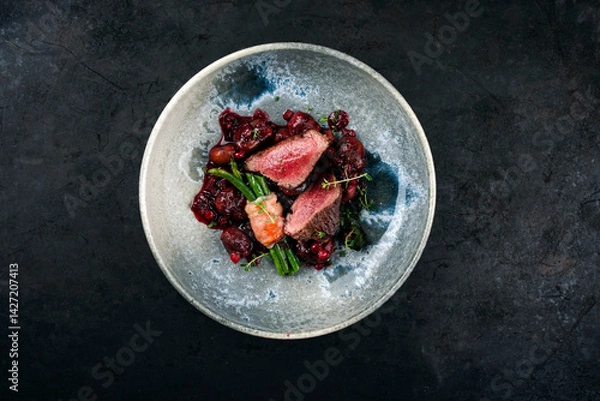 Obraz Traditionally roasted fillet of saddle of venison with chestnuts, bacon-wrapped bean sticks and redcurrants served with lingonberry sauce as top view in a bowl with a rustic background