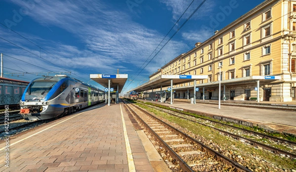 Fototapeta Cuneo, Piedmont, Italy - March 03, 2025: Cuneo Railway station with trains at the platform, regional rail transport of RFI - Rete ferroviaria Italiana (Italian Railway Network)