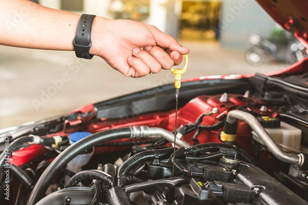 Fototapeta Man service mechanic maintenance inspection service maintenance car Check engine oil level car in garage showroom dealership blurred background.