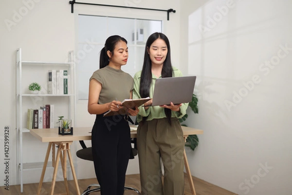 Obraz Portrait of Two Asian business woman standing in an office, holding documents and discussing work. Business ideas and strategies