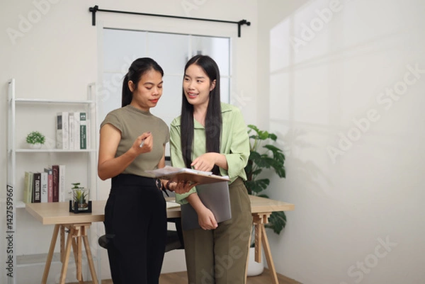 Obraz Portrait of Two Asian business woman standing in an office, holding documents and discussing work. Business ideas and strategies