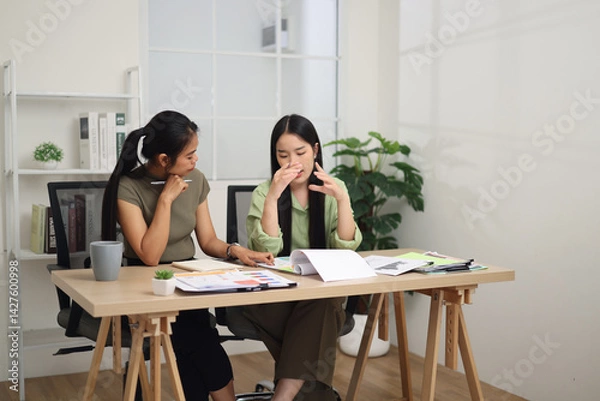 Obraz Portrait of Two female colleagues are sitting together at desk, reviewing documents and discussing work in the office.