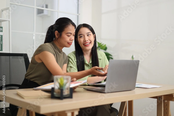 Obraz Portrait of Two Asian businesswoman are working together at a desk, discussing documents while looking at a laptop screen. Business ideas and strategies