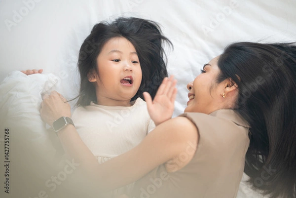 Fototapeta Top view of Asian mother and daughter cuddle and talking on bed. Family enjoy playing and spending time together at home
