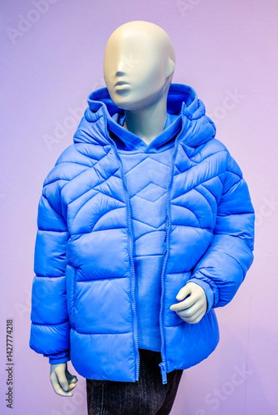 Obraz Shop display showcases a blue padded jacket worn by a mannequin in a clothing store located in Austria, highlighting modern fashion trends in winter apparel