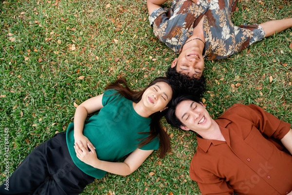 Obraz Three Friends Enjoying a Sunny Day in the Park, Relaxing on the Grass with Smiles and Joy, Embracing Friendship and Togetherness in Nature