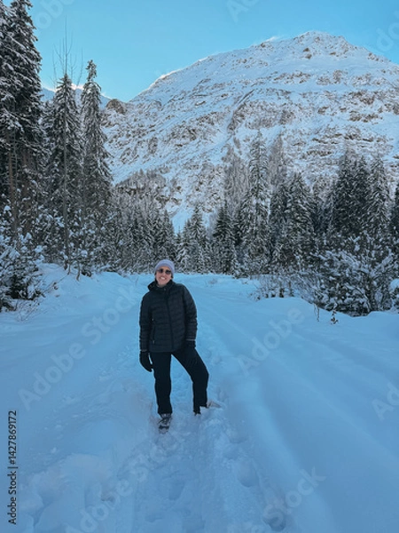 Fototapeta Hiker enjoying a scenic winter trek on a snowy mountain path, surrounded by snow-covered trees and a majestic peak