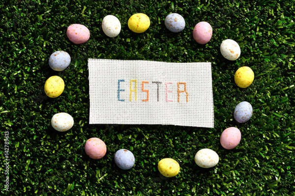 Fototapeta Easter cross stitched on textile isolated on artificial grass displayed with speckled eggs