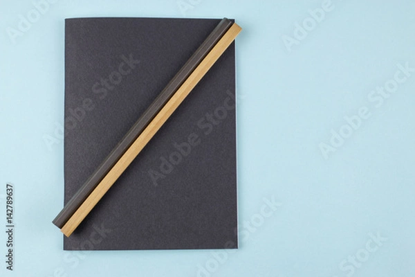 Fototapeta Black notebook and pencils on blue background.